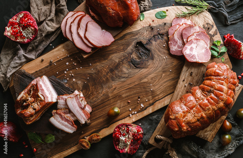 Obraz na płótnie Antipasto with cold meat, ham, sausage, salami, parma, prosciutto, bacon decorated with pomegranate, spices and herbs on wooden board over black background