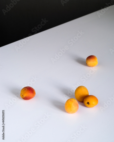 on a white background table scattered five ripe orange apricots isolated. daylight from the window to the right. the table stands diagonally in the upper left corner of a dark wall minimalism