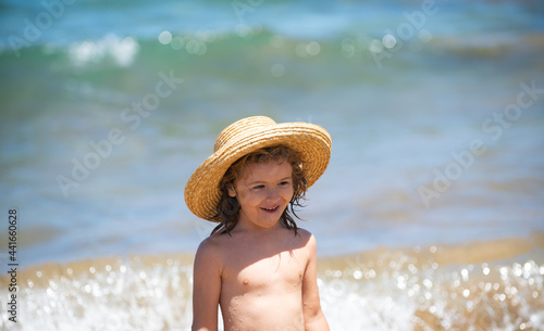Adorable little boy in straw hat at beach during summer vacation. Portrait of playful kid on the sea background. Funny summer child face.