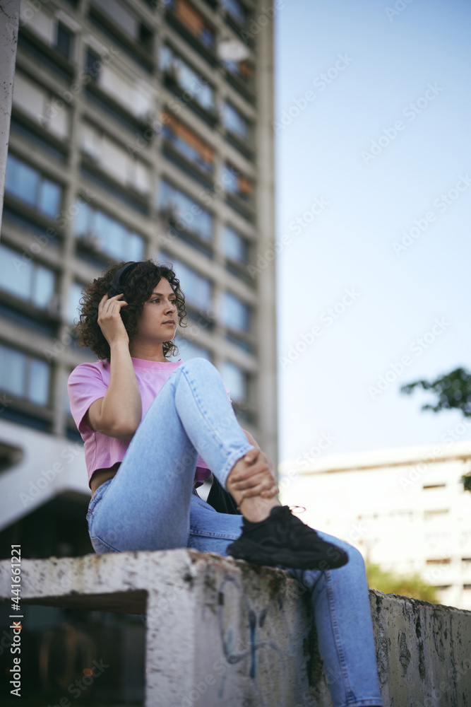 Cute young woman sitting outdoors with headphones on and listening to the music.