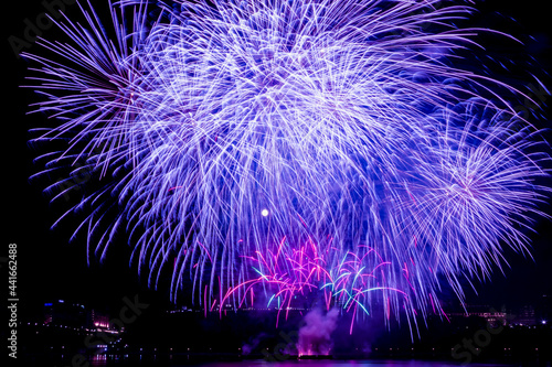 Purple fireworks fill the night sky over downtown skyline, with the full moon shining through
