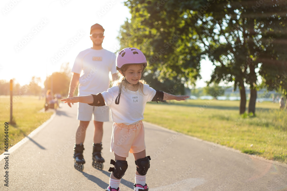 Fototapeta premium Child girl roller skating with dad in the park. Family time, activity, sport.