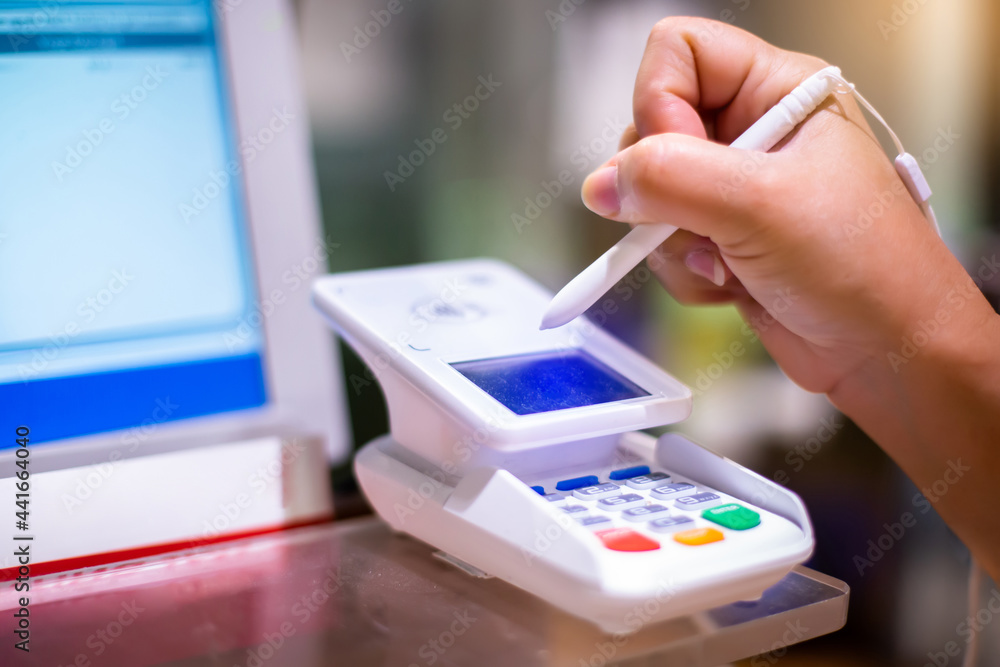 Selective focus to customer hand signing with electronic pen on a touch screen of credit card sale transaction receipt machine at supper market. Electronic signature concept. Selective focus to customer hand signing with electronic pen on a touch screen of credit card sale transaction receipt machine at supper market. Electronic signature concept.