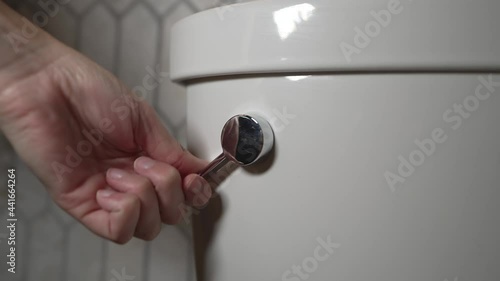 This slow motion video shows an anonymous hand flushing a toilet handle in clean and modern bathroom. photo