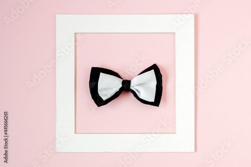 Black and white bow tie in a square white frame. Pink background. Copy space.