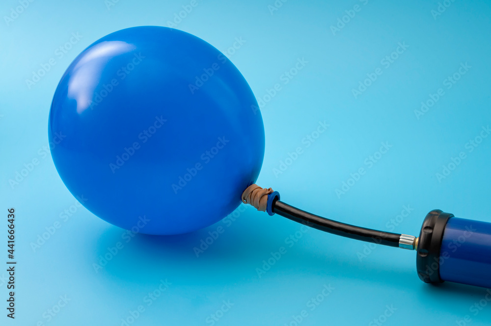 Party accessory, fun decoration and financial bubble with pump inflating a latex balloon isolated on blue background with copy space on the blank balloon
