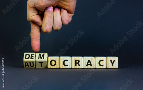 Democracy or autocracy symbol. Businessman turns wooden cubes and changes the word autocracy to democracy. Beautiful grey background, copy space. Business and democracy or autocracy concept. photo
