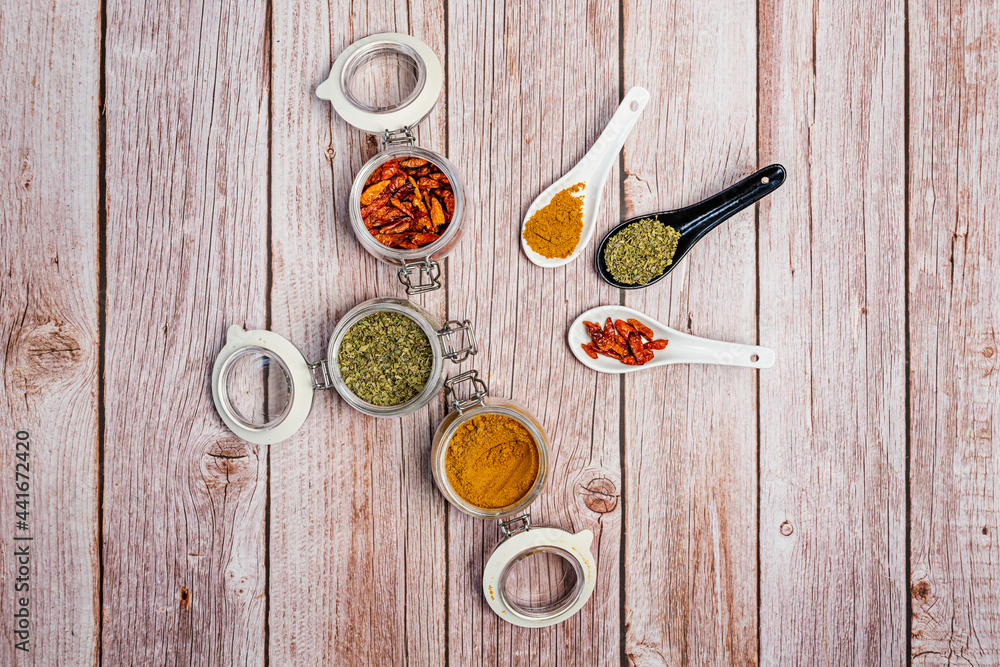 Open airtight spice jars and porcelain spoons filled with oregano, curry and cayenne Open airtight spice jars and porcelain spoons filled with oregano, curry and cayenne