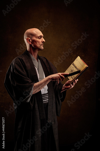View of a blind and bald man wearing a kimono holding a book in his hands
