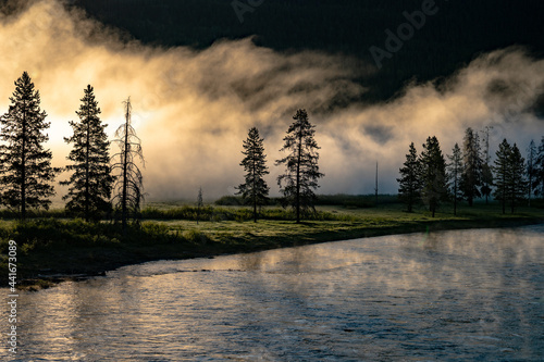 Landscape photo of fog hangs over trees along a river with light rays shining through in US National Park 09