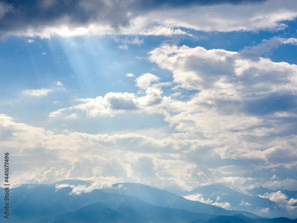 Obraz premium 6月下旬、雲間から差し込む光芒と山並みの風景