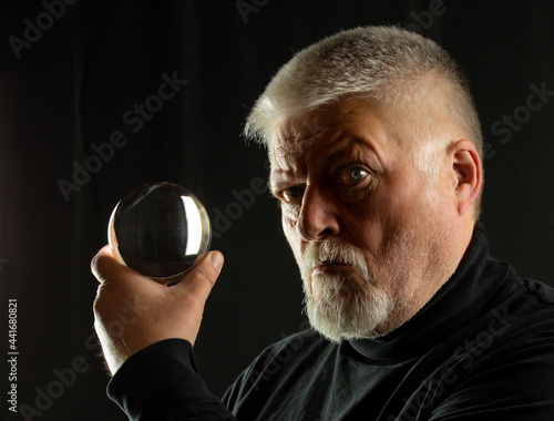 Porträt von einem Wahrsager mit Bart und grauen Haaren, der eine Glaskugel in der Hand hält. Der Hintergrund ist schwarz. photo