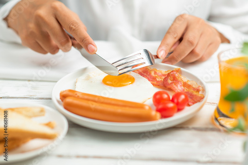 women holds a fork and knife eating breakfast.fried egg,sausage,bacon,toast bread,orange juice.