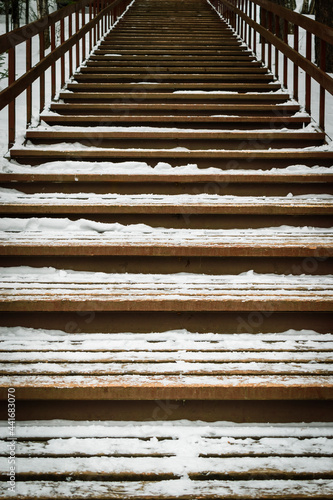 Gloomy wooden staircase in forest in winter. White snow on steps.