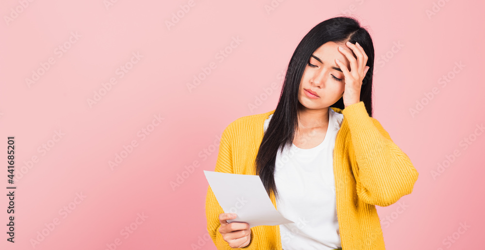 Portrait of beautiful Asian young woman sad tired strain holding paper calculating bills on hand, female person problem she hold worried over bill, studio shot isolated on pink background Portrait of beautiful Asian young woman sad tired strain holding paper calculating bills on hand, female person problem she hold worried over bill, studio shot isolated on pink background