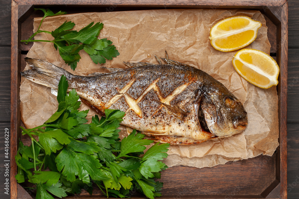 Baked dorado fish with lemon and parsley in a dish on the table. Top View Baked dorado fish with lemon and parsley in a dish on the table. Top View