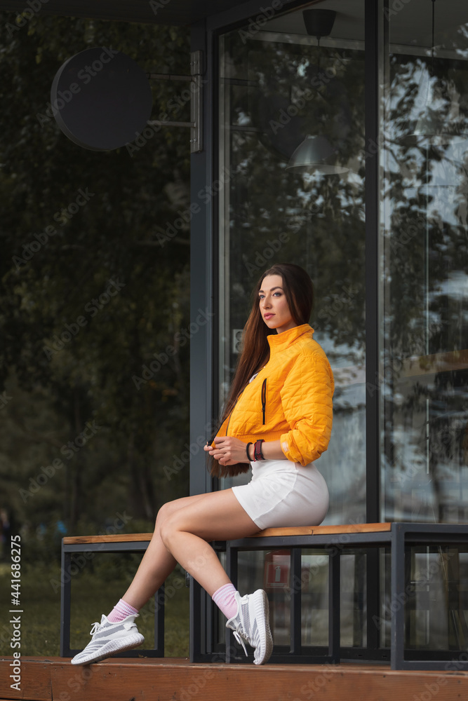 Fashion portrait of young trendy woman dressed in white dress .sits on bench, enjoy vacation  in the  green city park , autumn street fashion.  portrait of joyful woman