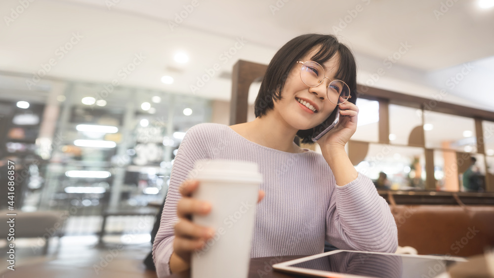 Young adult business asian woman short hair using mobile call and talking at indoor cafe on day.