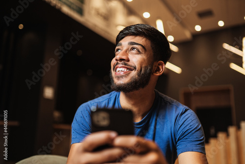 Photographie Young latin man using cell phone. Texting on cafe.