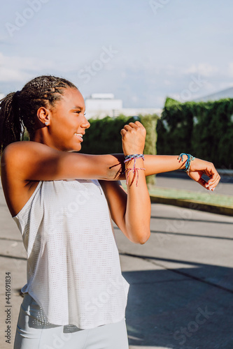 cheerful young african american woman doing arm stretching while smiling, sport life, sunny day, practicing sport