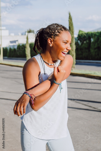 cheerful young african american woman doing arm stretching while smiling, sport life, sunny day, practicing sport
