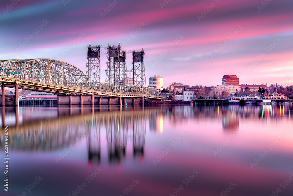 Obraz premium The I-5 Interstate Bridge at sunrise with purple and pink clouds reflecting in the Columbia River - Portland, Oregon to Vancouver, Washington