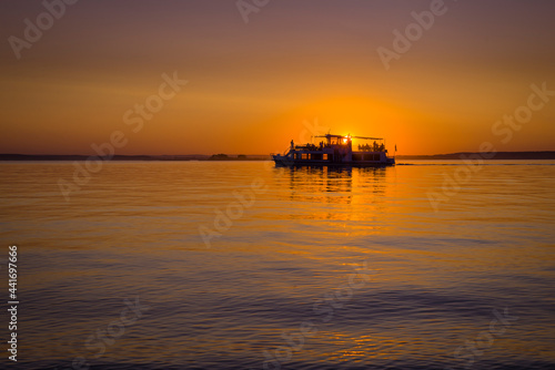 A small ship in front of setting sun.