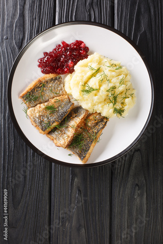 Swedish Stekt stromming or fried herring with boiled potatoes and lingonberry jam closeup in the plate on the table. Vertical top view from above