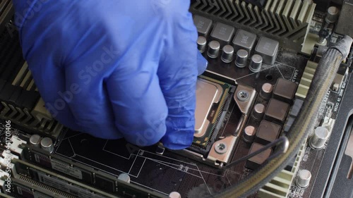Electronics repair technician with a blue glove carefully installs a computer processor into a socket on the motherboard of a desktop computer. View from the inside of a personal computer system