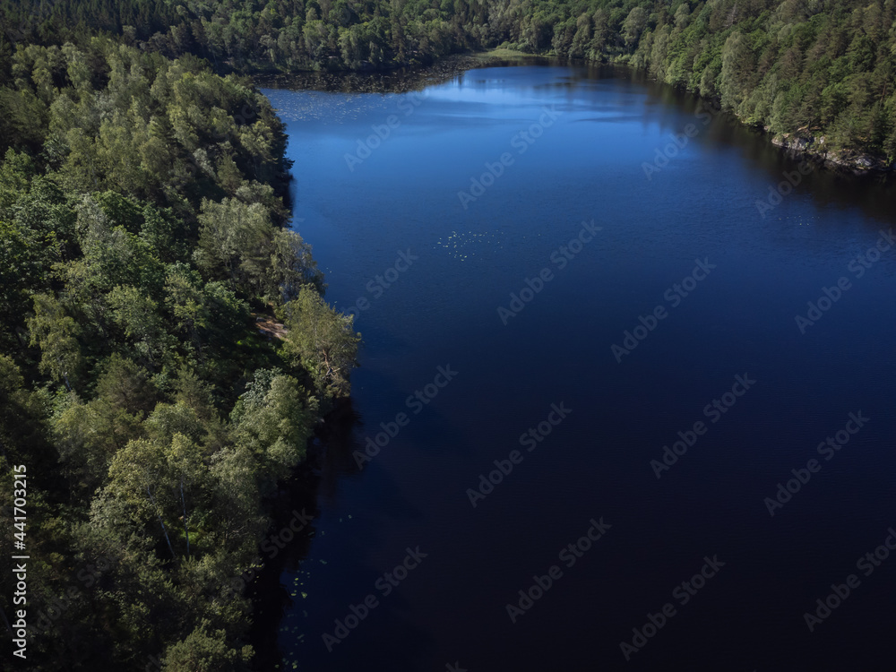 Bird's eye view of a pond, lake with green trees. Aerial, drone nature photography taken from above in Sweden in summer.  Dark blue water surface background with copy space and place for text.