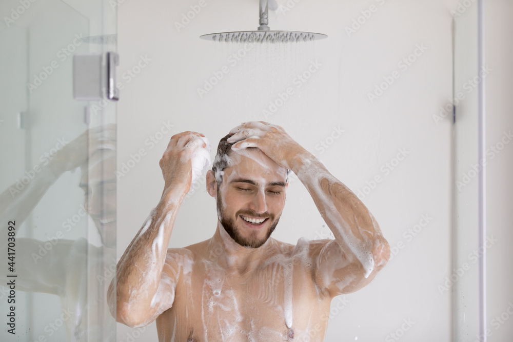 Happy attractive muscular guy taking shower, washing head, hair with