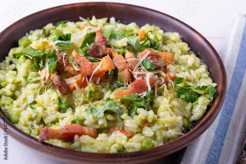 Homemade risotto with peas and fried crispy bacon, pancetta and grated cheese on a plate, close-up