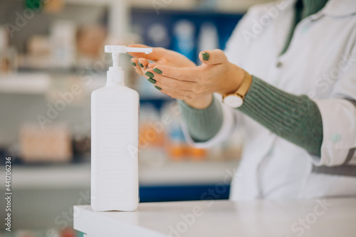 Young woman pharmacist desinfecting hands with sanitazer photo