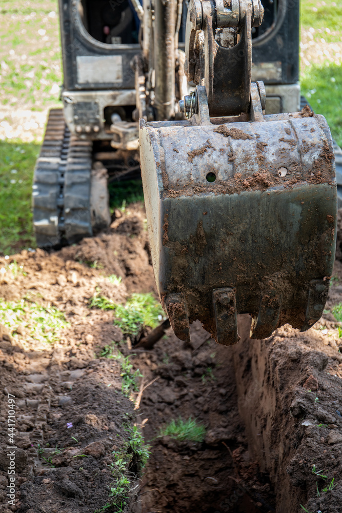 Fototapeta premium Mini excavator digs a pit or trench for communications