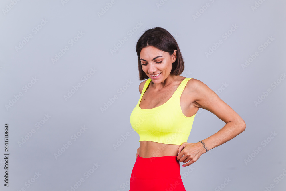 Sports woman stands on gray background, demonstrating her abs, satisfied with the results of fitness training and diet, has a happy facial expression, wears a sports top and tight leggings Sports woman stands on gray background, demonstrating her abs, satisfied with the results of fitness training and diet, has a happy facial expression, wears a sports top and tight leggings