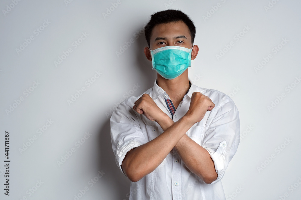 Portrait of young asian man standing and hand crossed in front of her chest posing like he ready to protect from the virus against white background. Symptoms of contracting corona virus concept Portrait of young asian man standing and hand crossed in front of her chest posing like he ready to protect from the virus against white background. Symptoms of contracting corona virus concept