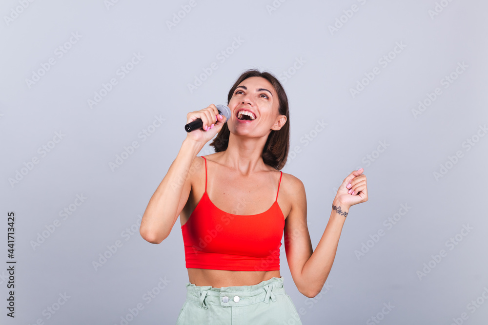 Beautiful woman on gray background with microphone singing emotional favorite song happy positive cheerful Beautiful woman on gray background with microphone singing emotional favorite song happy positive cheerful