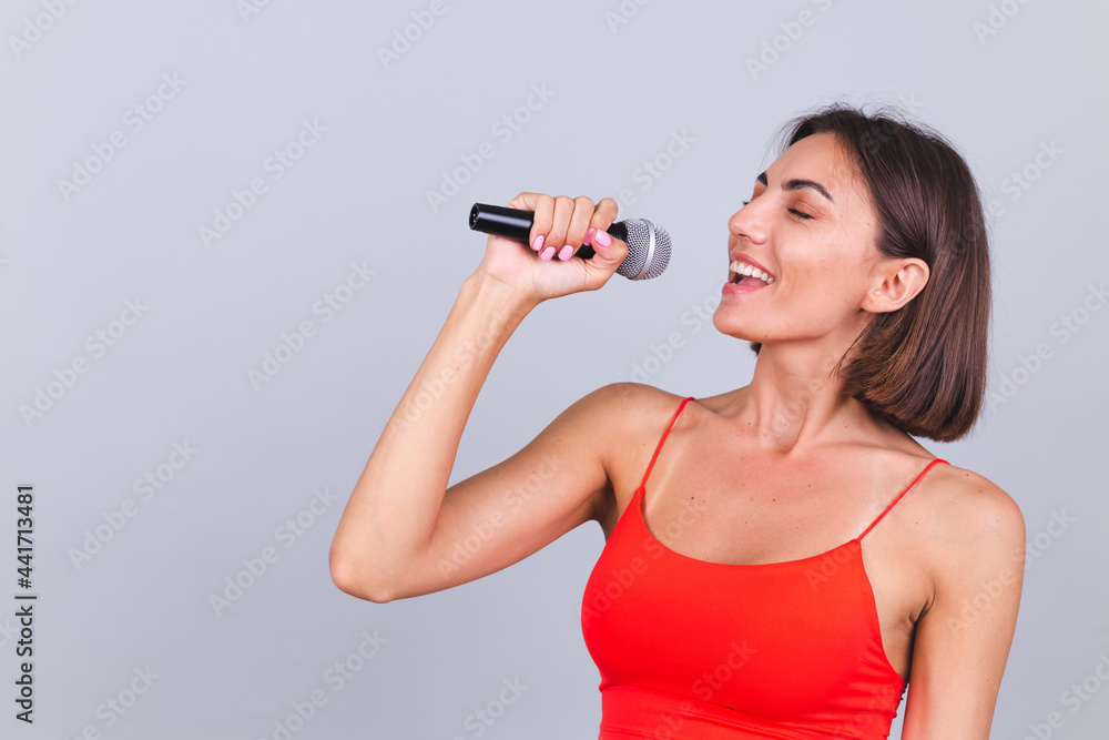 Beautiful woman on gray background with microphone singing emotional favorite song happy positive cheerful Beautiful woman on gray background with microphone singing emotional favorite song happy positive cheerful