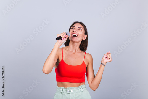 Beautiful woman on gray background with microphone singing emotional favorite song happy positive cheerful