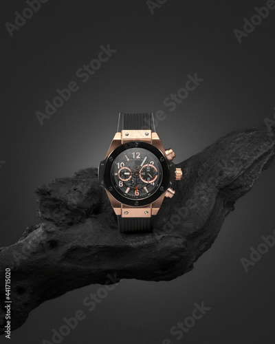 Beautiful gold men's watch with a black strap on a wooden stand, on a gray background. Beautiful gold watch. A luxury brand watch photo