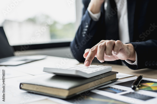 A man in a suit is pressing a calculator, a business man sitting in a private office at a company, he runs a startup company, he is a young man who starts a business. Startup company concept.