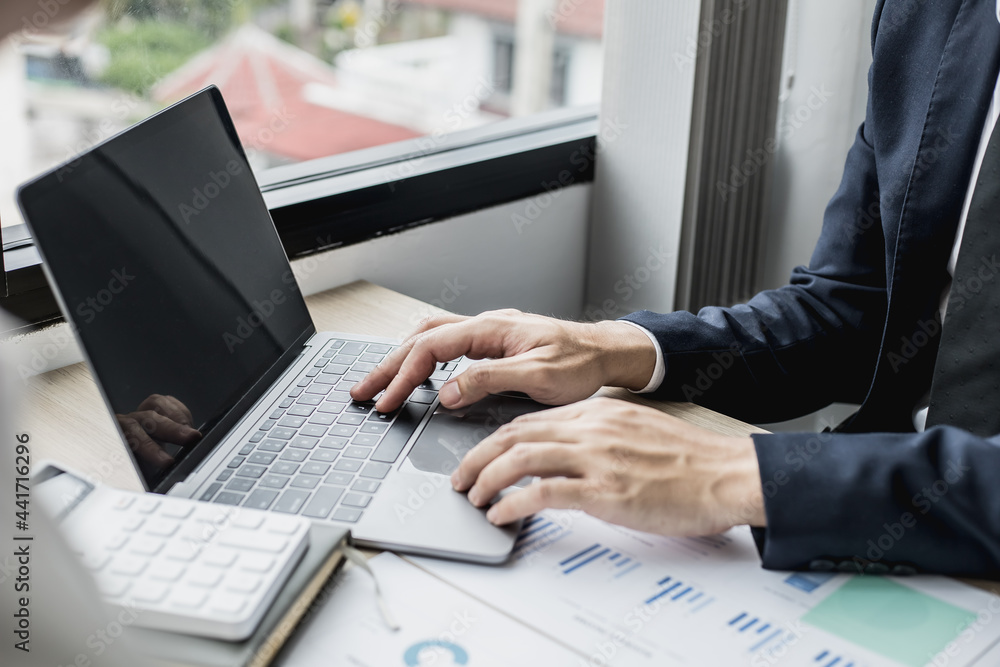 Fototapeta premium Man in suit sitting at work and using a laptop, he is a young businessman who founded a startup, he is typing text messages with his partner through an online messenger on his laptop.
