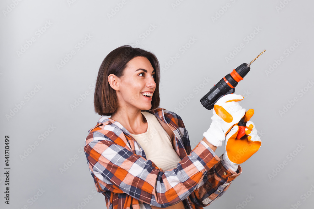 Beautiful woman in plaid shirt on gray background holds drill to repair home confident happy smile Beautiful woman in plaid shirt on gray background holds drill to repair home confident happy smile