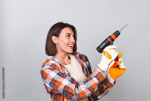 Beautiful woman in plaid shirt on gray background holds drill to repair  home confident happy smile