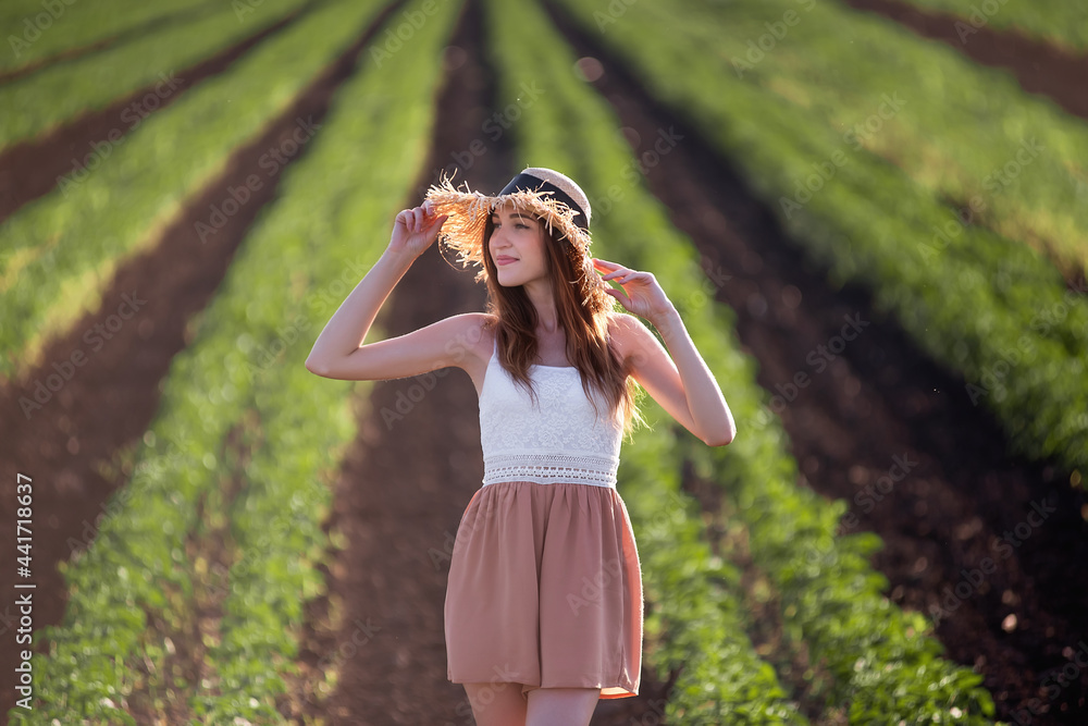 Young woman in white T-shirt, powdery shorts runs along green plowed field. Long hair develops at sunset, the girl has straw hat. Promote agricultural perspective, the texture of black soil ground Young woman in white T-shirt, powdery shorts runs along green plowed field. Long hair develops at sunset, the girl has straw hat. Promote agricultural perspective, the texture of black soil ground