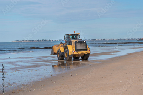 A construction excavator prepares a beach in Brittany for the arrival of tourists 