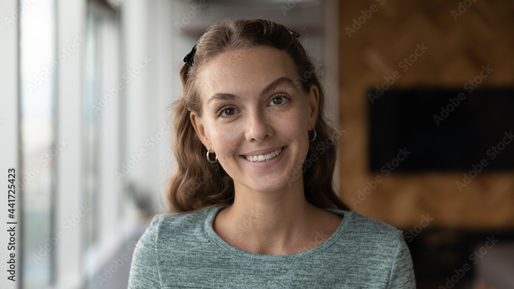 Head shot portrait of smiling young 20s woman, posing in modern office room. Happy millennial business lady employee worker holding video call, professional corporate career opportunity concept.