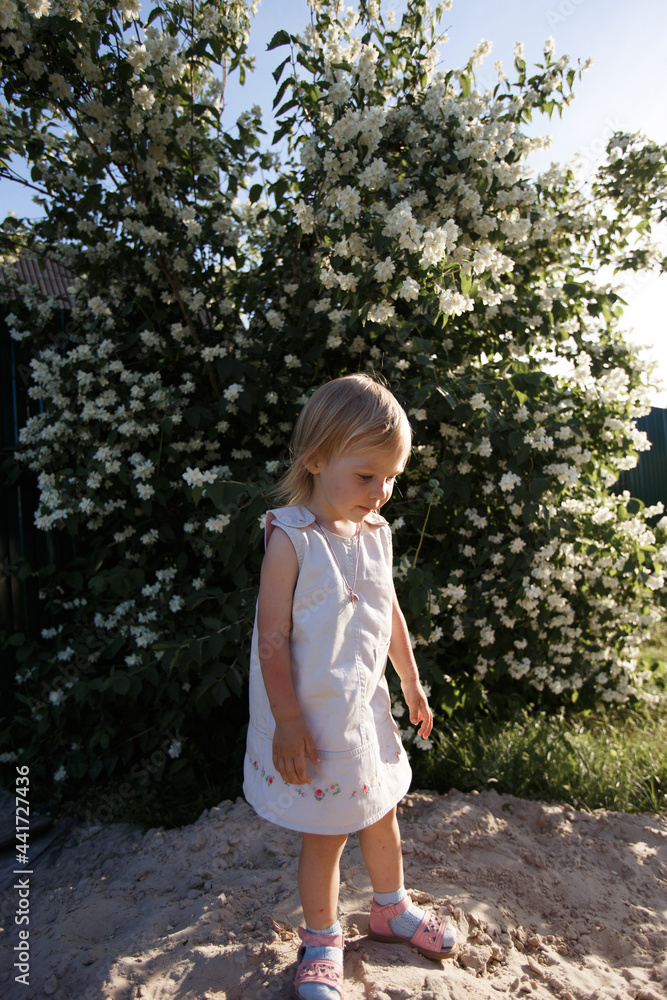 a little girl in a light dress stands on a mountain of sand and looks down a little girl in a light dress stands on a mountain of sand and looks down