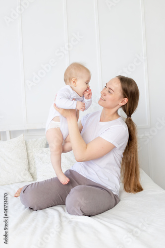 happy mom holds a baby in her arms lifting it up on the bed at home