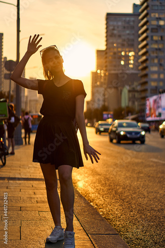 A young slim woman in the summer stands against the sun. Summer parties. An adult girl walks in the city on the streets in black clothes. Urban ordinary style.